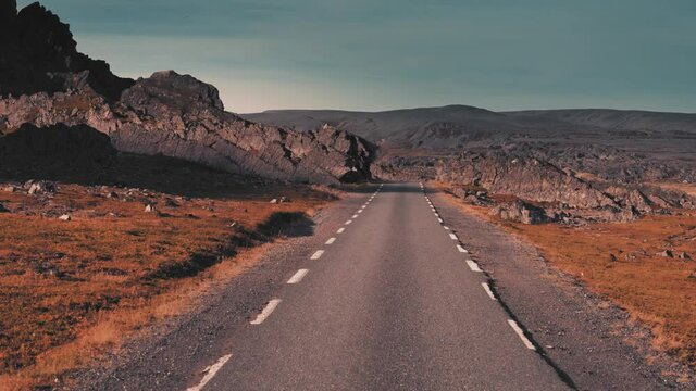 Dolly zoom. The narrow road leads through the desolate outlandish landscape.