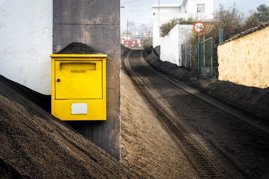 A yellow mailbox surrounded by volcanic ash.