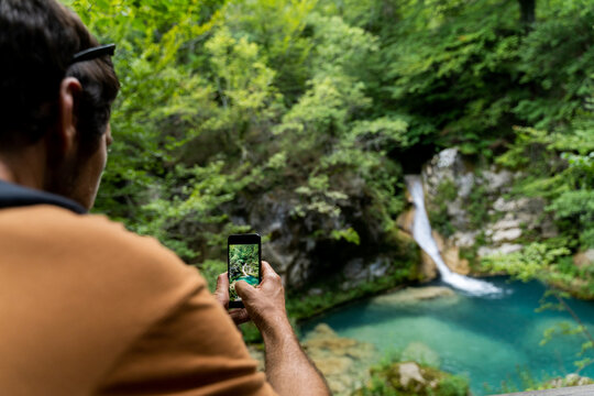 Back view of man taking photo of waterfall in nature