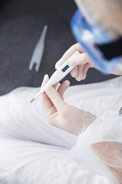 Crop physician measuring temperature of patient