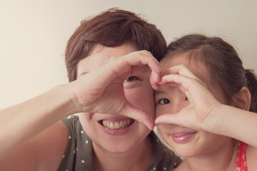 Asian mother and daugther girl making heart shape gesture with hands over eyes , Happy volunteer...