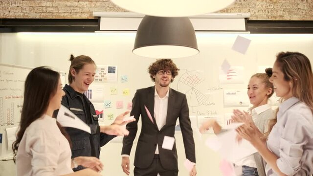 Happiness young multiracial coworker's team celebrates business success with Caucasian boss by throwing papers and clapping, cheerful when the meeting finishes in an office's conference workplace.