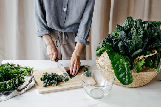 Crop woman cutting kale on chopping board