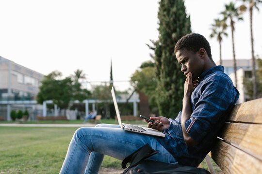 Thoughtful guy with gadgets on park bench