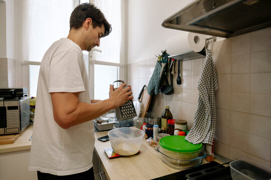 Man uses a grater while preparing food in the kitchen. 