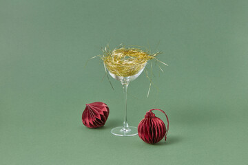 Glass with gold tinsel and red baubles on background