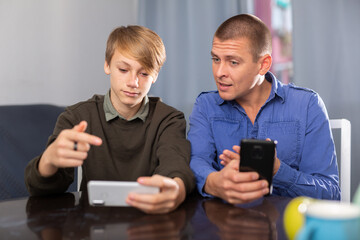 Father and son together playing on their smartphones while sitting at the table at home