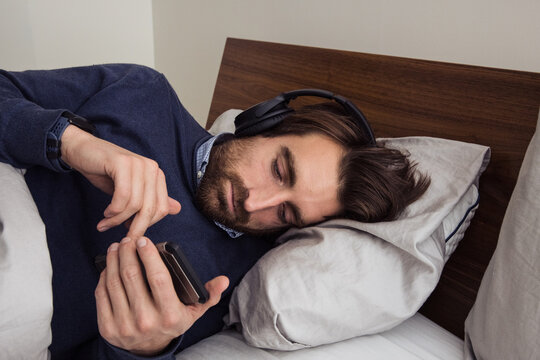 Man in headphones uses his phone laying in bed