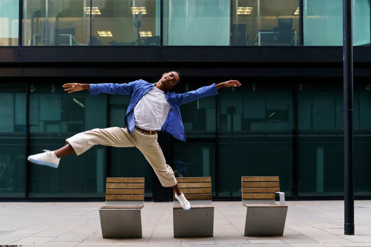 Stylish man dacing and jumping over street bench