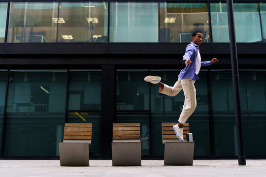 Stylish man dacing and jumping over street bench