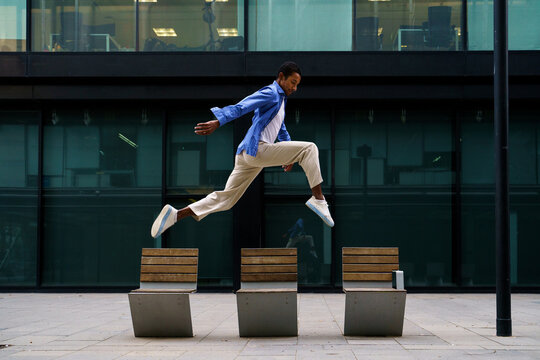 Stylish man dacing and jumping over street bench