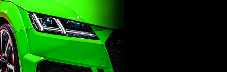 Front view of the LED headlights modern green car on black background, copy space
