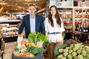Adult couple is standing with cart with products in the supermarket