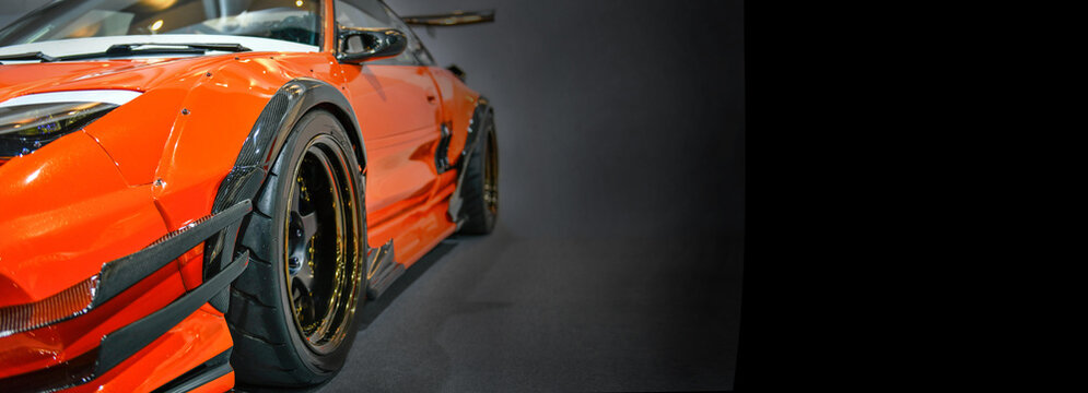 Front headlights of orange modify car on black background, copy space