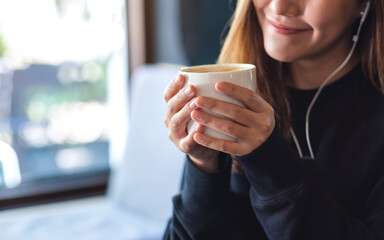 Closeup of a young woman drinking coffee while putting on an earphone to listen to music