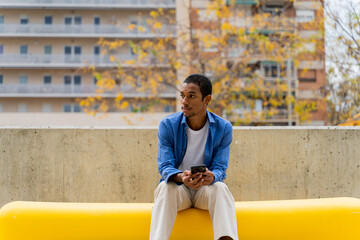 Trendy man sitting on bench and using phone