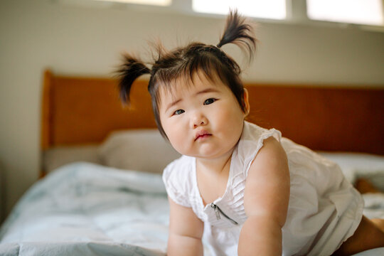 Close up of Asian baby with pigtails on bed