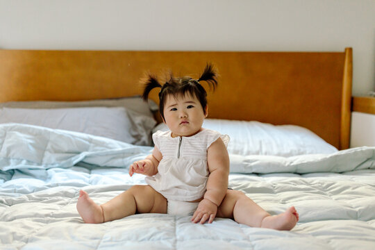 Beautiful Asian baby with pigtails on bed