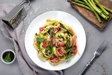 Pasta with asparagus and prosciutto on gray background.