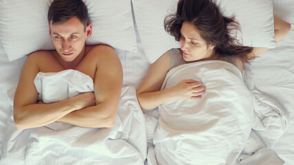 Obraz na płótnie Canvas Couple husband and wife expecting baby argue lying in soft bed covered with white sheets and man took offense after waking up in morning at home, upper view.