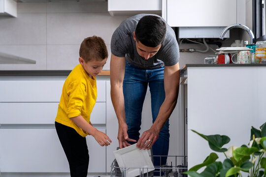 son watching his dad place the dishes in the dishwasher