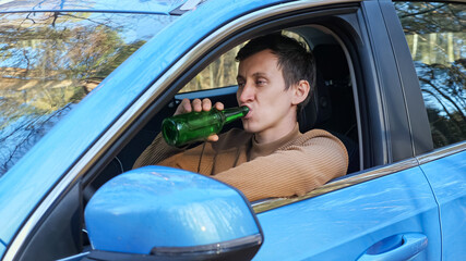 Driver with brunet short hair sits in car cabin and drinks alcohol from glass bottle tired after hard work day, resting in auto parked by forest