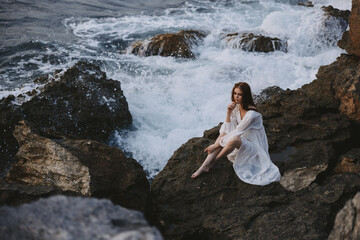 barefoot woman in white dress sits on a stone with wet hair unaltered