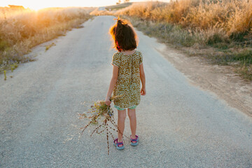 Bak of kid with wild flowers in hand at sunset o