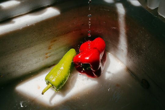 Red and green peppers under tap water in the sink