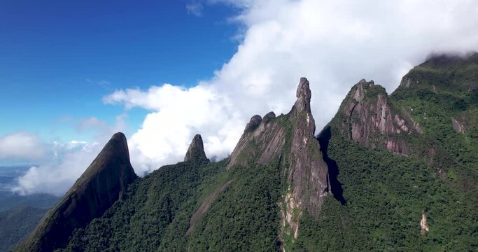 Aerial slow approach in Brazilian panoramic landscape of mountain range Serra dos Orgaos in Teresopolis, Rio de Janeiro with Dedo de Deus, Gods finger, peak in the middle and clouds behind