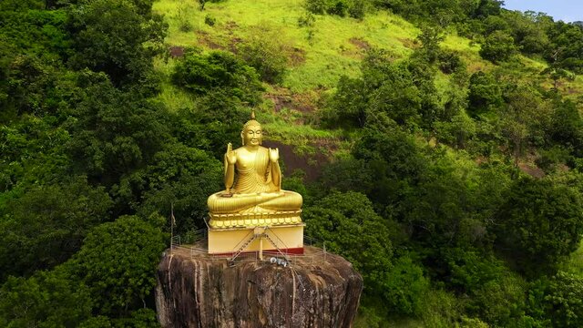 A statue of a seated golden Buddha on a rock in a mountain temple. Aluvihara, Matale, Central Province, Sri Lanka.