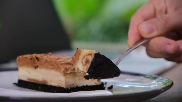 Close up of human hands tapping on laptop and eating tasty cake slice in coworking cafe, freelance lifestyle concept 