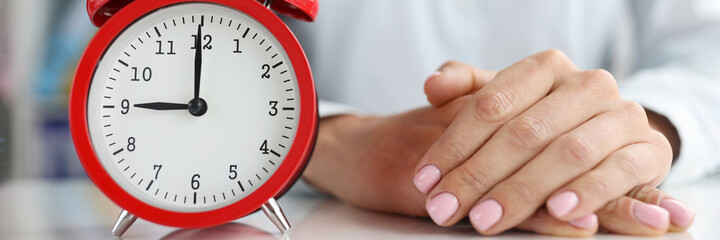 Red alarm clock at nine in morning and the businessman sits with folded arms at table