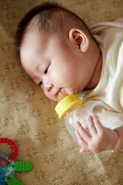 Closeup of Asian baby biting milk bottle

