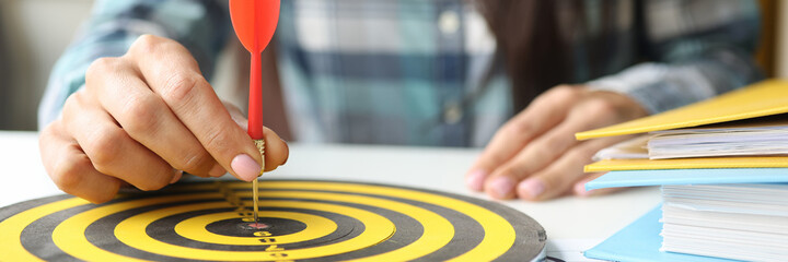 Businesswoman puts dart in center of darts at workplace in office