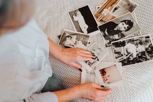 Memories of childhood, nastolgiya of youth concept. Close-up of caucasian woman looking at her baby vintage photo while sitting on sofa, indoors. Selective focus on monochrome retro pictures, top view