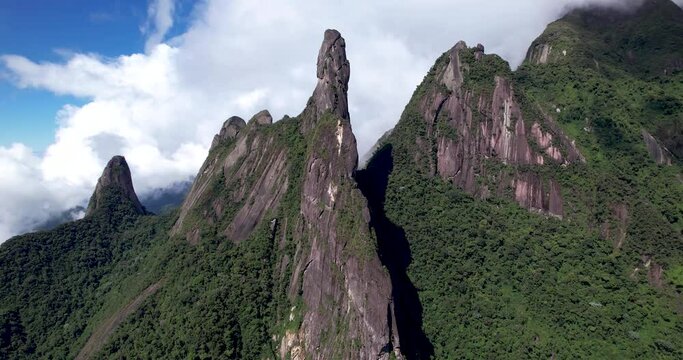 Aerial slow panning panorama landscape of mountain range Serra dos Orgaos in Teresopolis, Rio de Janeiro, Brazil, with God's finger peak in the middle and clouds behind