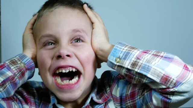 Emotions of the child. A 6-7 year old boy holds his head and depicts anger, horror, fright, screams