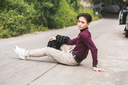 A Young Asian Man In A Purple Turtle Neck Sweater And Khaki Pants Sitting In The Middle Of The Road.