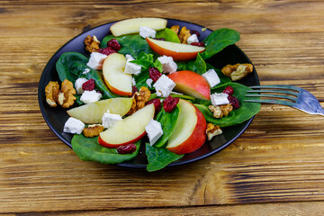 Autumn spinach salad with apple, feta cheese, walnut and dried cranberry on wooden table. Healthy vegetarian food