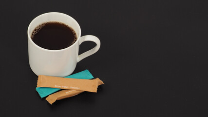 Hot coffee in white cup  and sugar sachets isolated on black background.