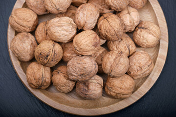 Group of walnuts on a black background. Nuts on a wooden plate close-up. Walnut on black top view copy space.