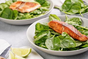Grey bowl with fresh green raw spinach and fried red salmon, lime slices on grey concrete surface