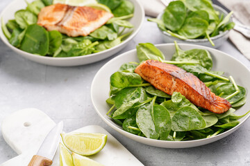 Grey bowl with fresh green raw spinach and fried red salmon, lime slices on grey concrete surface