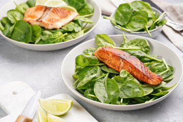Grey bowl with fresh green raw spinach and fried red salmon, lime slices on grey concrete surface