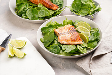 Grey bowl with fresh green raw spinach and fried red salmon, lime slices on grey concrete surface