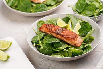 Grey bowl with fresh green raw spinach and fried red salmon, lime slices on grey concrete surface