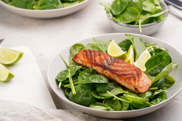 Grey bowl with fresh green raw spinach and fried red salmon, lime slices on grey concrete surface