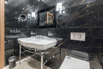 Stylish bathroom with walls decorated with black marble tiles, with a mirror over the original sink.