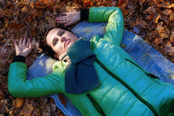 An adult motionless woman in an autumn jacket, in a scarf, lies on the ground with dry leaves, eyes...